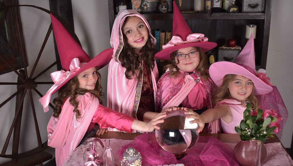 young girls dressed in pink Halloween costumes with hands on crystal ball
